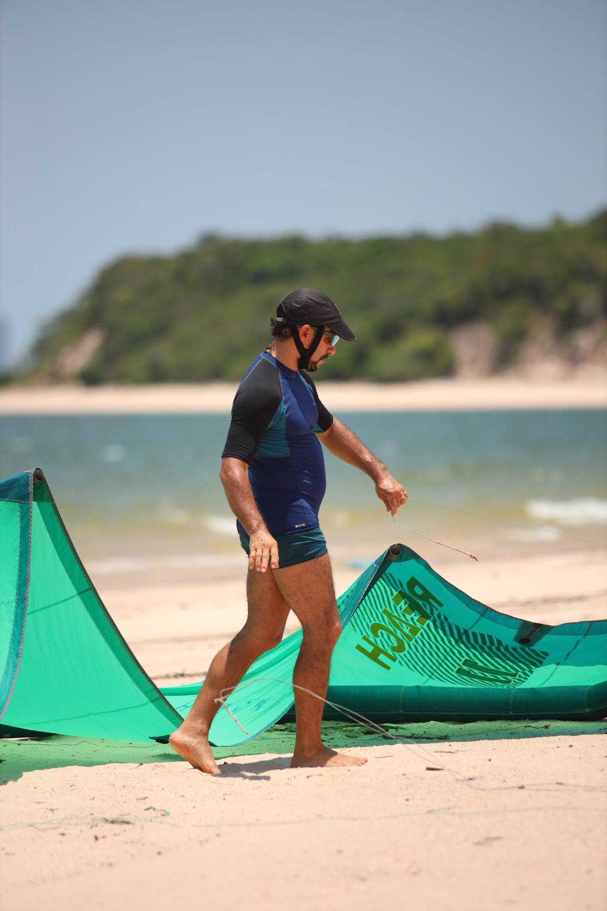 Kitesurfista com a pipa verde na praia, com a floresta ao fundo